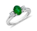 A three stone emerald engagement ring of the May birthstone centered between two round-cut diamonds on either side set in white gold