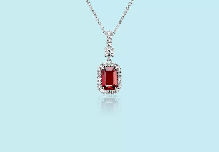 A July birthstone pendant featuring an emerald-cut ruby framed in diamond pavé and topped with an additional princess-cut diamond and diamond studded bail set in white gold and matching chain