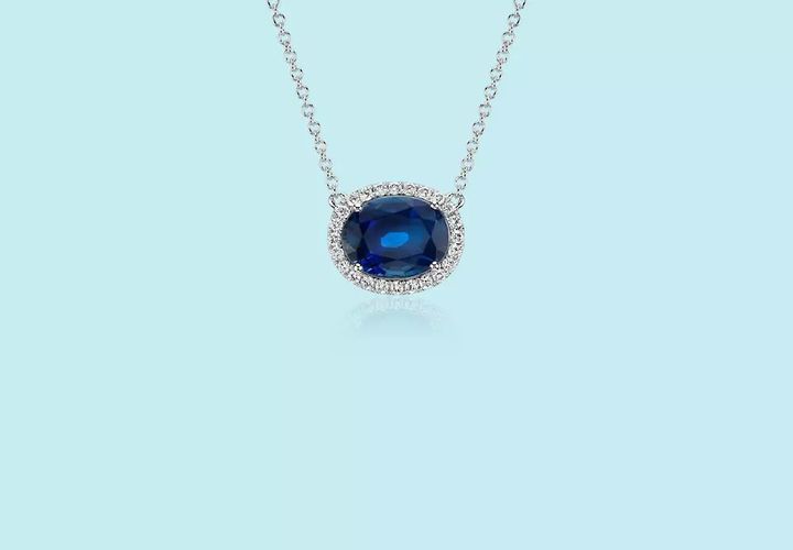 A September birthstone necklace of a large three-carat East-West set sapphire gemstone framed by pavé-set diamonds in white gold and chain