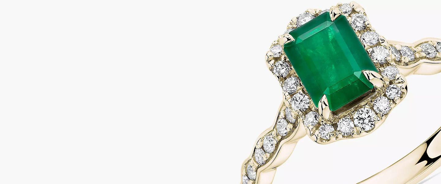 An emerald engagement ring ornamented by diamonds and gold filigree