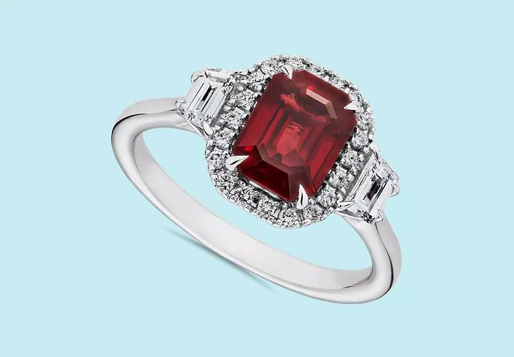 A ruby engagement ring accented with diamond halo and trapezoid diamond side stones set in white gold