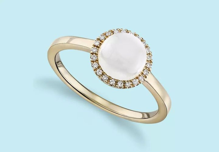 A round cabochon moonstone engagement ring circled in diamond halo and set in yellow gold
