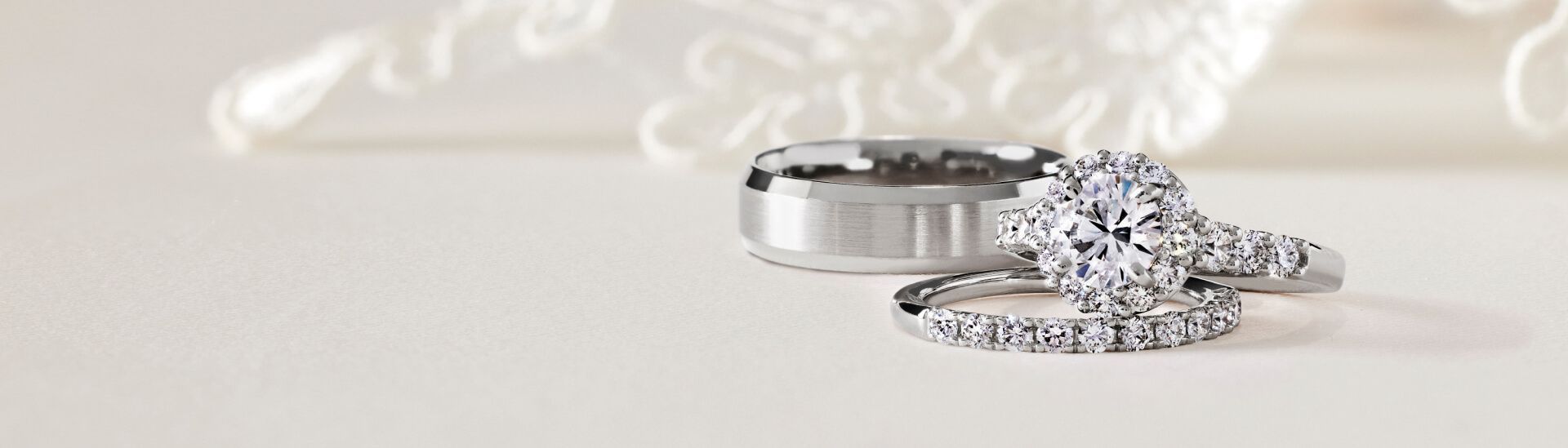 Two diamond rings and a plain metal band on a light background