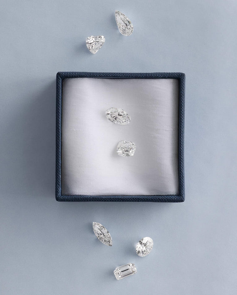 Various diamond cuts displayed in and around a blue box on a soft surface.