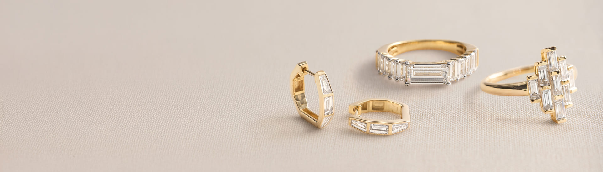 Gold rings and earrings adorned with baguette-cut diamonds on fabric surface.