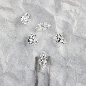 Five diamonds of various shapes on a textured gray background with tweezers.