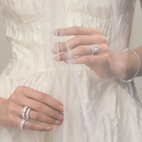 Bride's hands with diamond rings holding a delicate veil over her wedding dress.