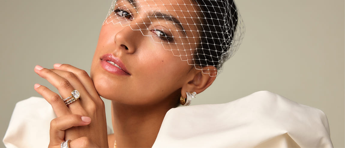 Woman wearing elegant jewelry and a netted veil, showcasing rings and earrings.