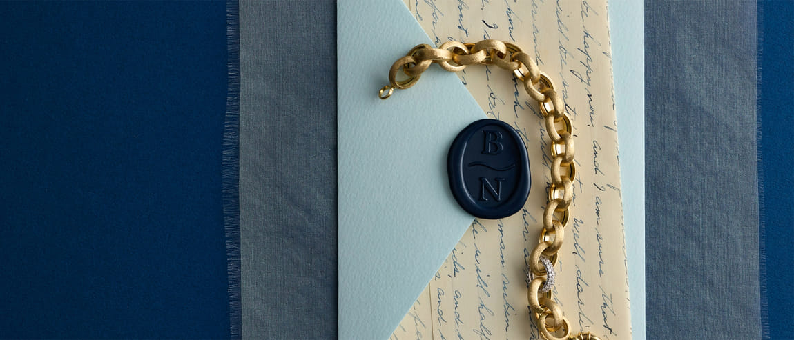 Gold link bracelet on blue paper with wax seal and handwritten script background.