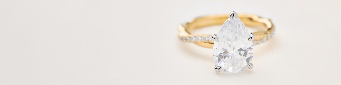 Pear-shaped diamond ring with a gold band on a light background.