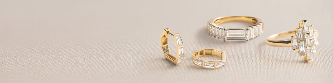 Collection of gold rings with rectangular and round diamond settings on a neutral fabric background.