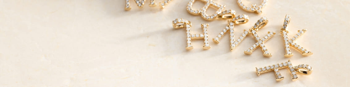 Scattered gold letter pendants with sparkling stones on a light surface.