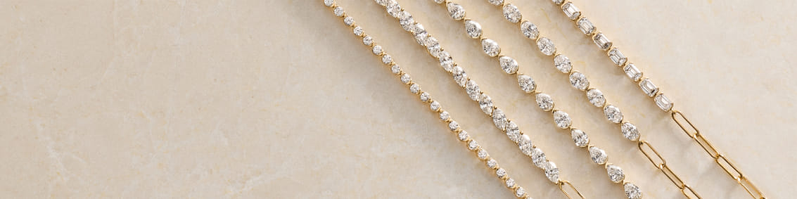 Gold bracelets with varying diamond shapes on a marble surface.