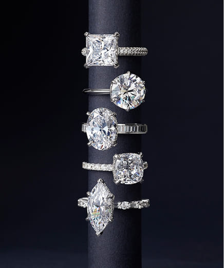 Collection of six diamond engagement rings displayed on a dark stand.