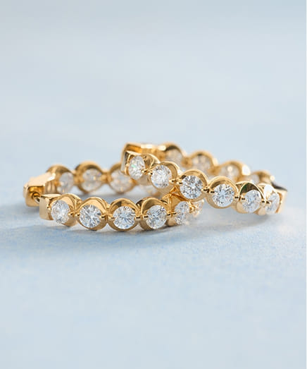 Gold hoop earrings with embedded round diamond gemstones on a light blue background.