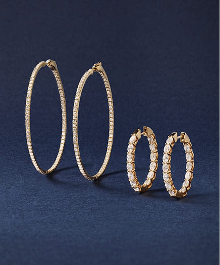 Two pairs of gold hoop earrings with embedded diamonds on a dark blue background.