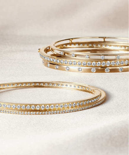 Elegant gold bangles studded with small gemstones on a soft fabric background.