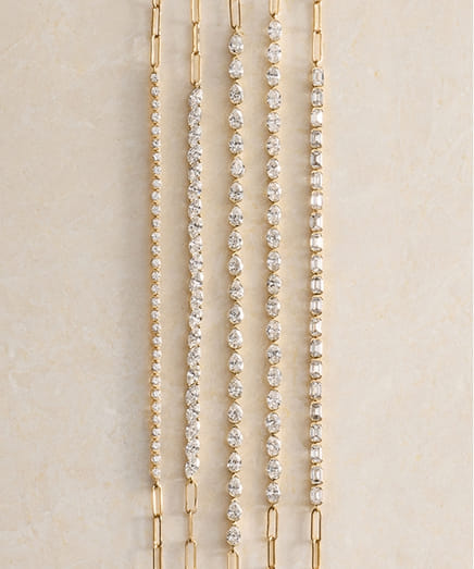 Five gold chain necklaces with diamond accents arranged vertically on a light surface.