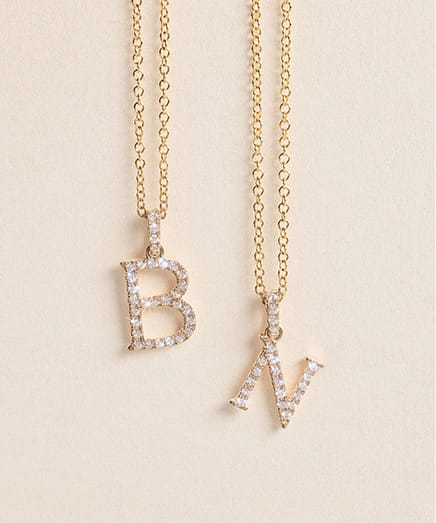 Gold necklaces with sparkling letter pendants B and N on a light background.