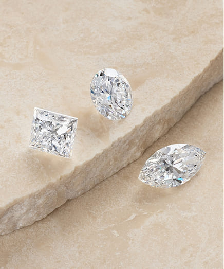 Three cut diamonds displayed on a textured beige surface