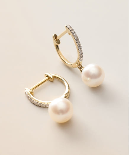 Gold hoop earrings with pearls and small diamonds on a light background.