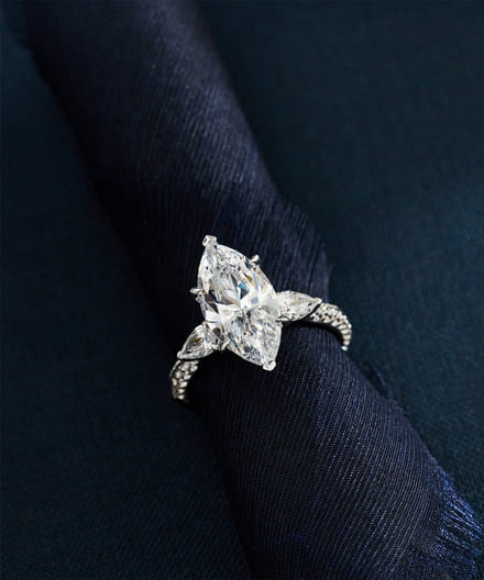 Elegant diamond ring with a detailed band on navy fabric background.