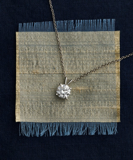Elegant diamond pendant necklace on textured blue fabric background.