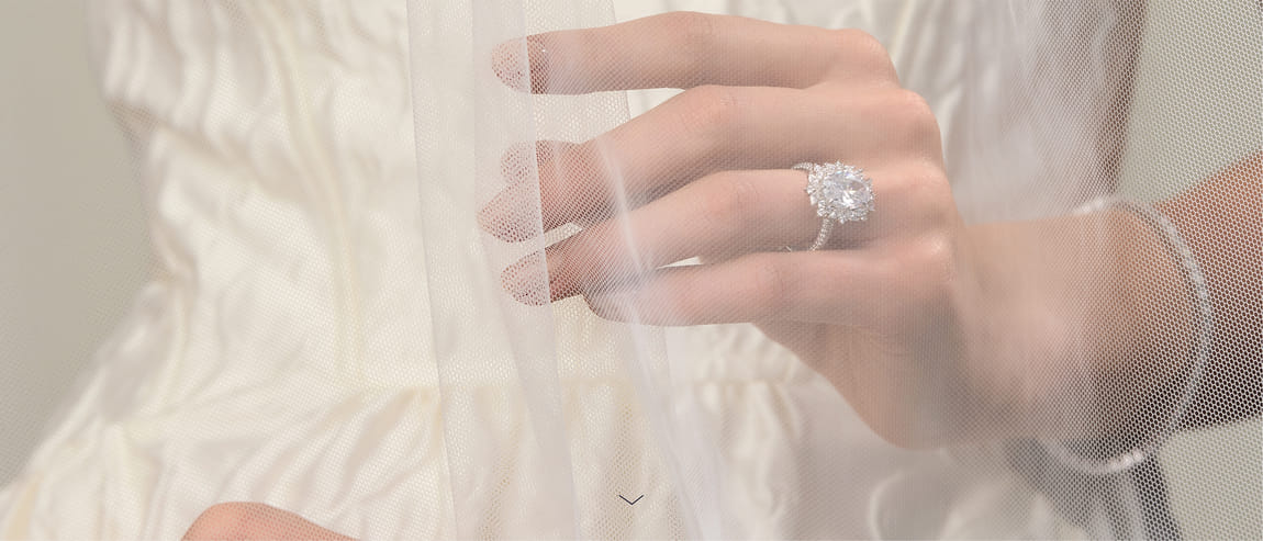 Close-up of hands with diamond rings, veiled in delicate white fabric.