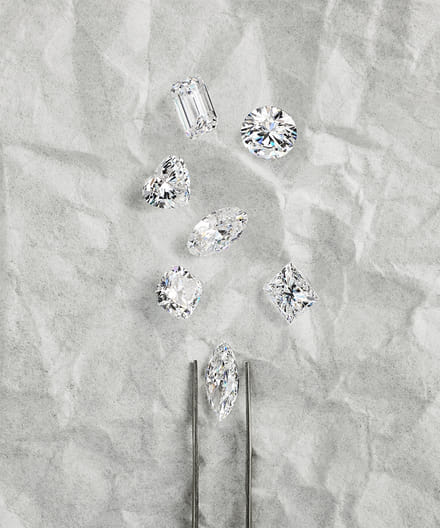 Various diamond cuts on a textured gray background with tweezers.