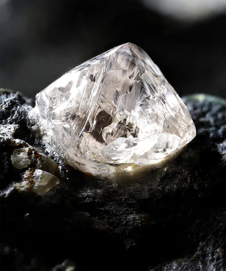 Close-up of a rough, uncut diamond on a dark textured background.