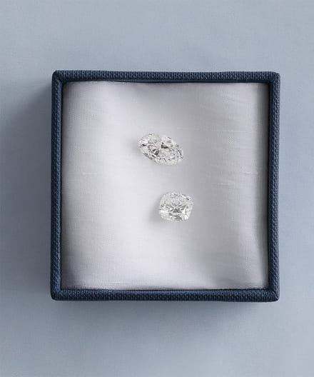 Two sparkling diamonds in a blue jewelry box on a soft fabric background.