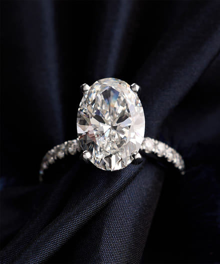 Elegant diamond ring with large oval stone and intricate band on dark fabric.