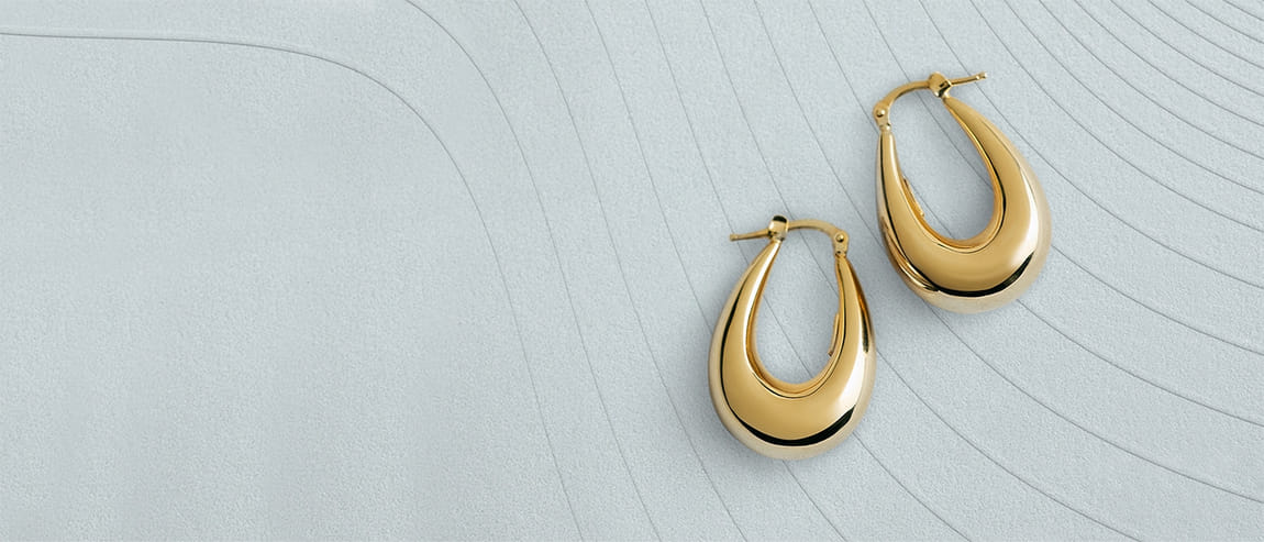 Pair of gold hoop earrings on textured gray surface with curved lines.