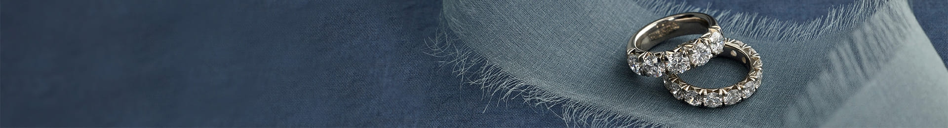 Pair of diamond rings on frayed blue fabric backdrop.