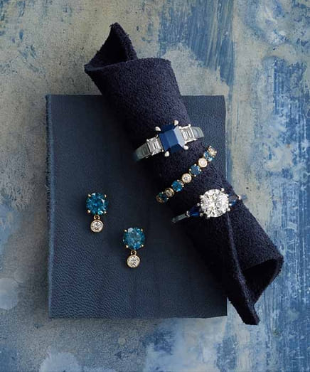 Elegant rings and earrings with blue gemstones arranged on a blue textured surface.