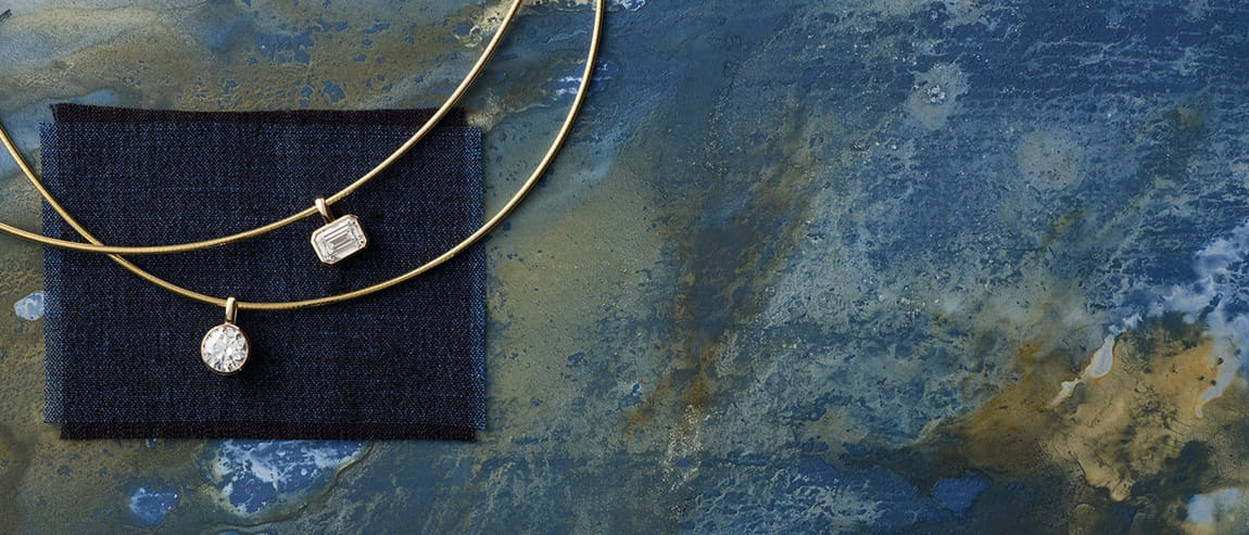Gold necklaces with diamond pendants on a blue textured surface.