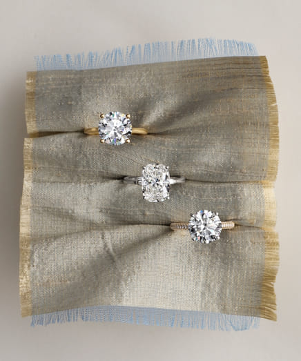Three diamond rings in different settings displayed on textured fabric.