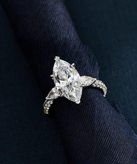 Elegant diamond ring with marquise cut centerpiece on dark textured fabric.