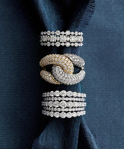 Elegantly stacked diamond rings on a dark blue fabric background.
