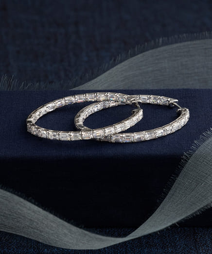 Elegant diamond hoop earrings on a dark fabric background.