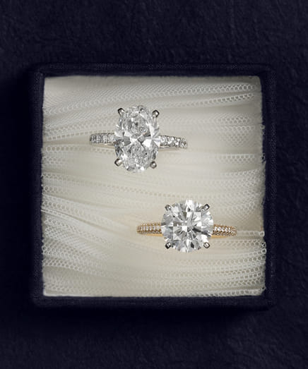 Two diamond engagement rings displayed in a box with a dark background.