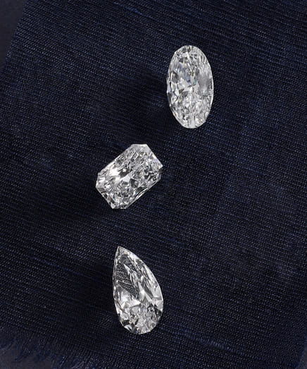 Three sparkling diamonds on a dark fabric background.