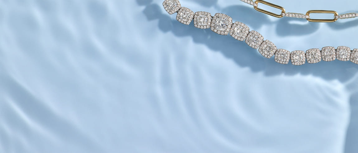 Diamond and gold necklaces on a light blue rippled surface.