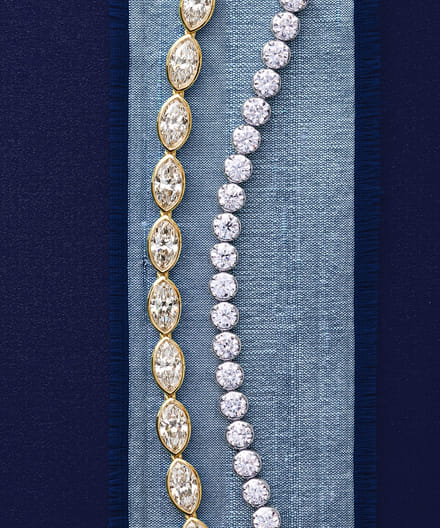 Two sparkling diamond bracelets on a blue fabric background.