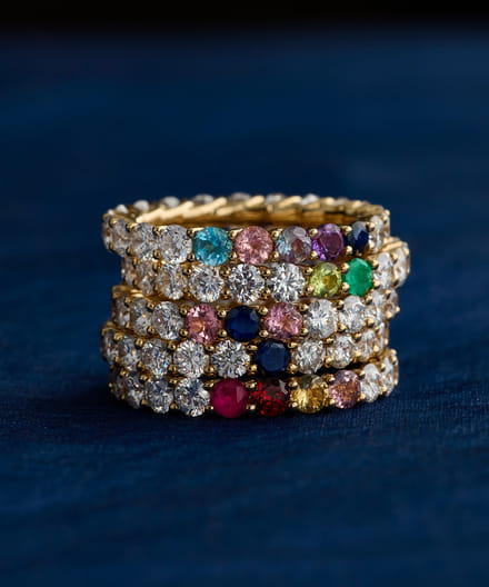 Stacked gold rings with colorful gemstones on a blue background