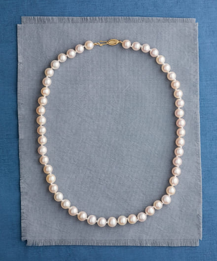 Elegant strand of pearls on a layered blue fabric background.
