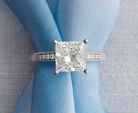Square diamond ring with detailed band on blue fabric background.