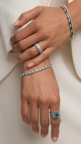 Hands wearing a silver ring with blue gemstone and coordinating bracelets.