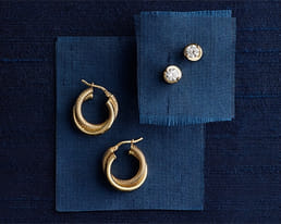 Gold hoop earrings and diamond studs on blue fabric squares.