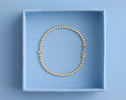 Gold diamond bracelet in a blue box with a heart detail on one link.